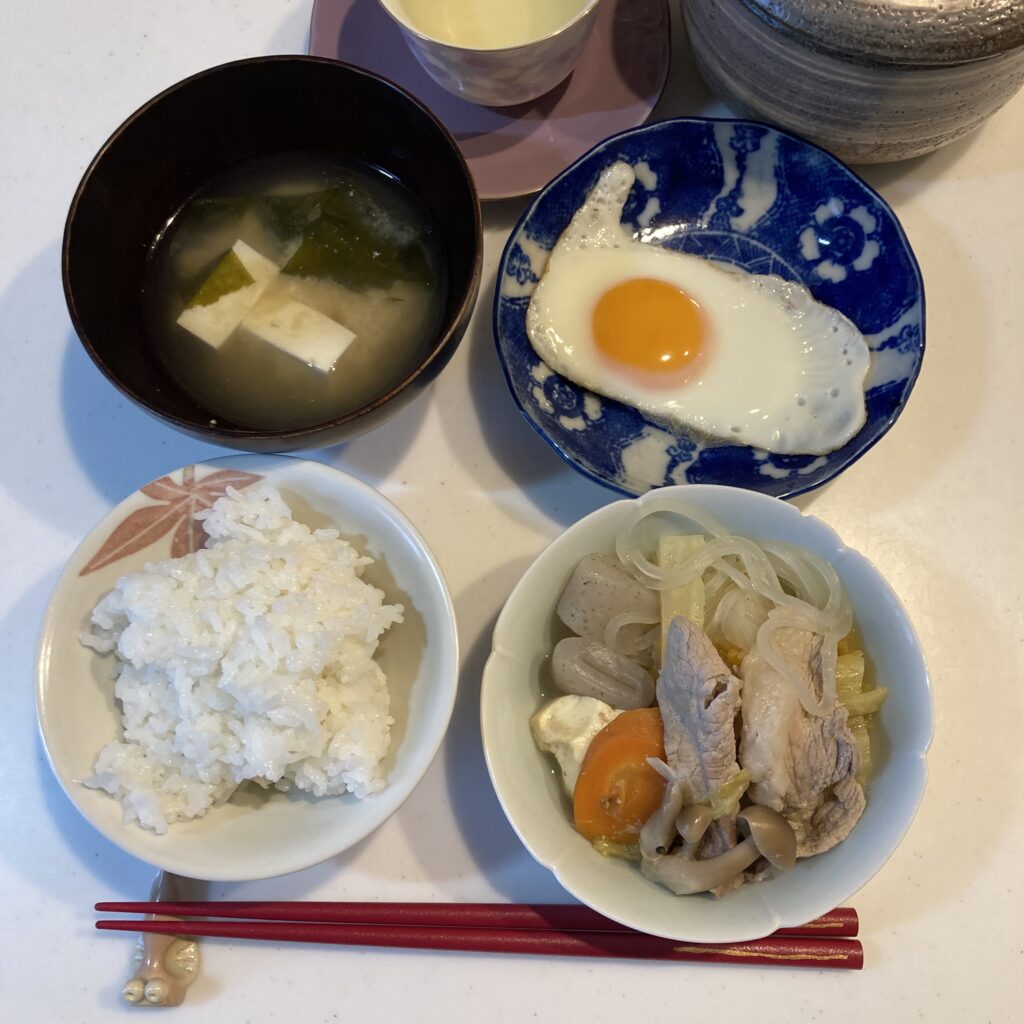 白いご飯と味噌汁、目玉焼きに、白菜たっぷりの鍋の残りを添えた朝ごはんの食卓。
