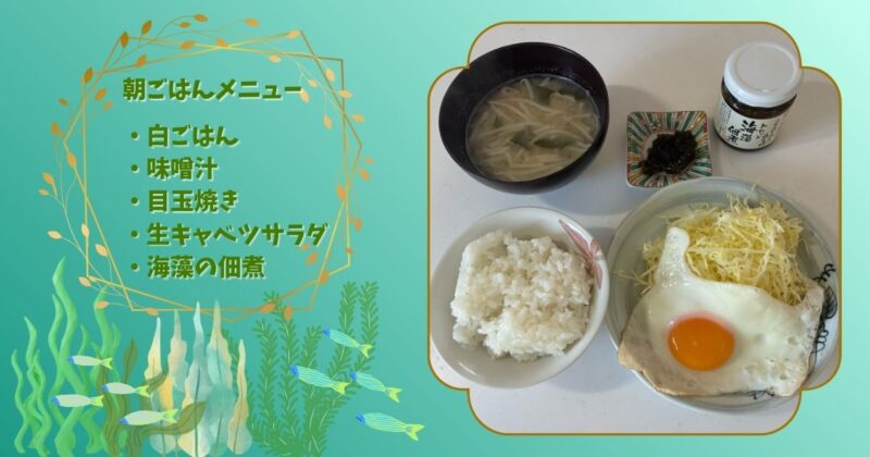 朝ごはんの写真。白ごはん、味噌汁、目玉焼き、生キャベツサラダ、海藻の佃煮が並び、メニュー文字と海藻のイラストが添えられている。