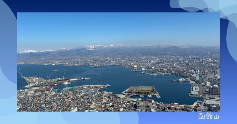 函館山山頂から見た函館湾のパノラマ。港に停泊する船と市街地、雪をかぶった山々が広がる